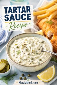 Bowl of thick homemade tartar sauce with pickle and herb flecks served beside crispy fish, chips, lemon, and fresh herbs