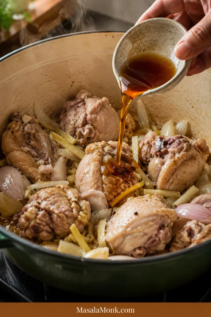 Fish sauce being poured into a pot with bone-in chicken, ginger, garlic, and onion before any broth is added.