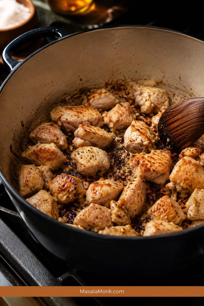 Boneless chicken thigh pieces browning in a Dutch oven with golden edges and browned bits on the bottom.