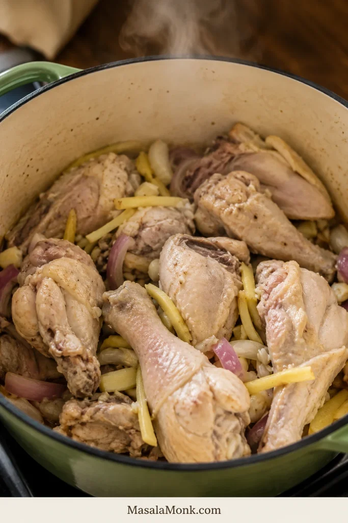 Bone-in chicken pieces cooking with sliced ginger, garlic, and onion in a pot before broth is added.