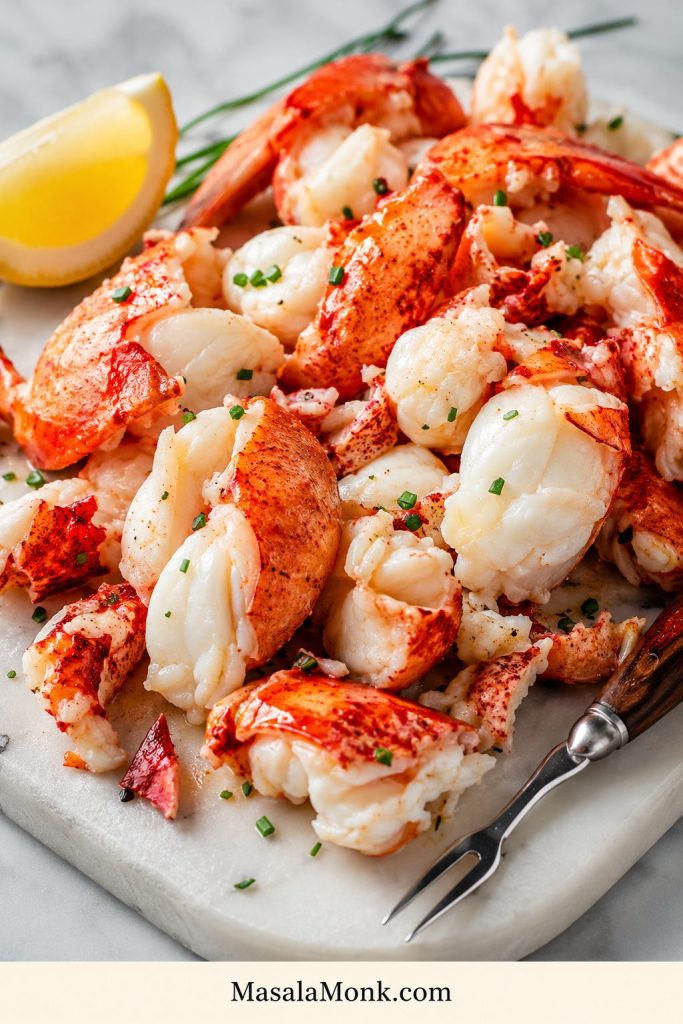 Large chopped lobster pieces on a board with herbs and lemon, ready to be added to mac and cheese.