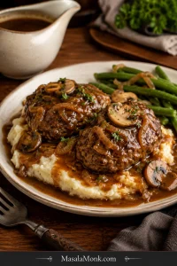 Two Salisbury steak patties covered with mushroom onion brown gravy over mashed potatoes, served with green beans on a cream plate.