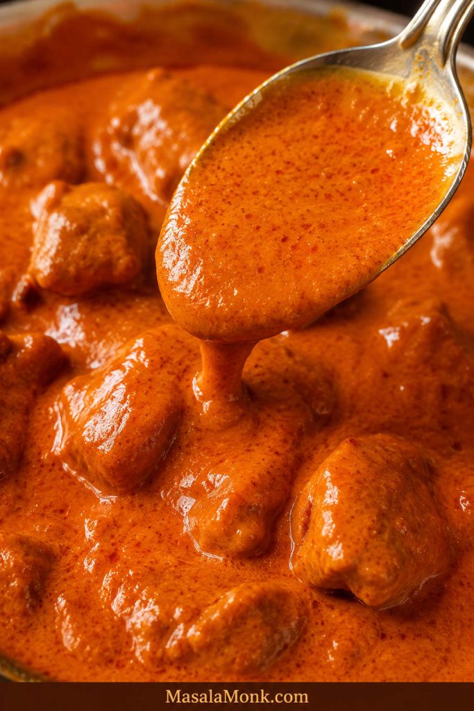 Close-up of finished chicken paprikash sauce coating chicken and a spoon with a glossy red-orange texture.