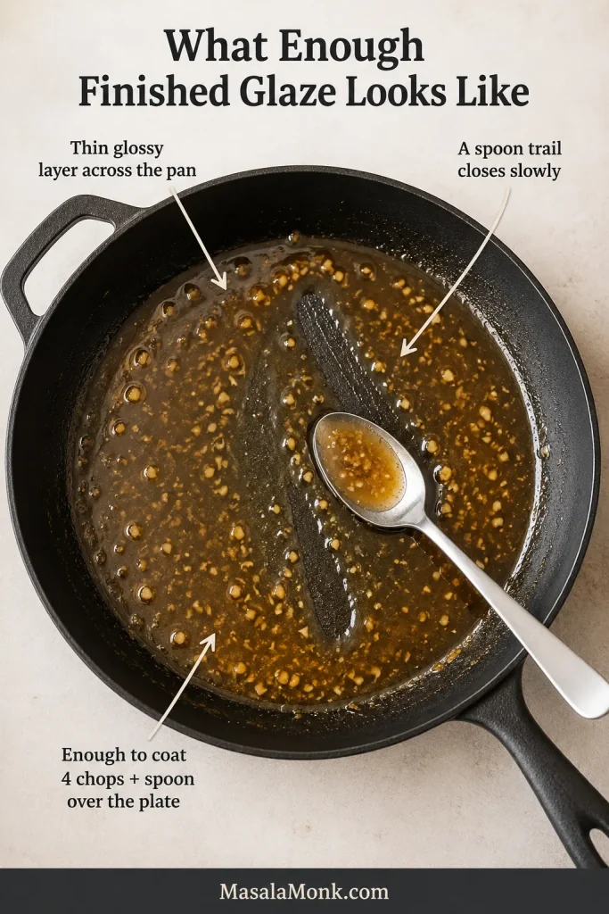 Overhead skillet coated with a shallow layer of honey garlic glaze, visible chopped garlic and a spoon trail through the center.