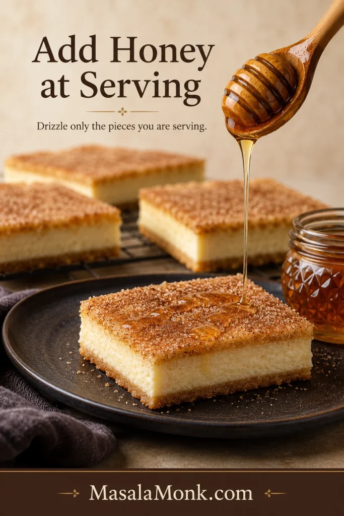 Thin stream of honey falling onto one plated Sopapilla Cheesecake bar, with undrizzled bars visible in the background.