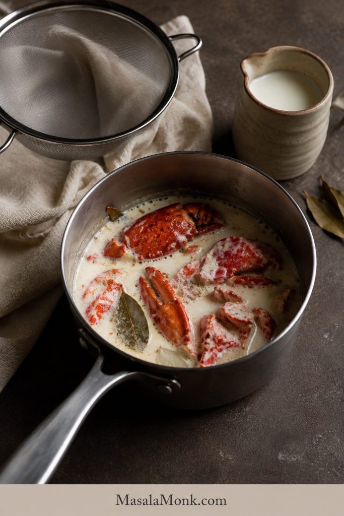 Lobster shells simmering in milk or cream with a bay leaf, with a strainer and pitcher nearby.