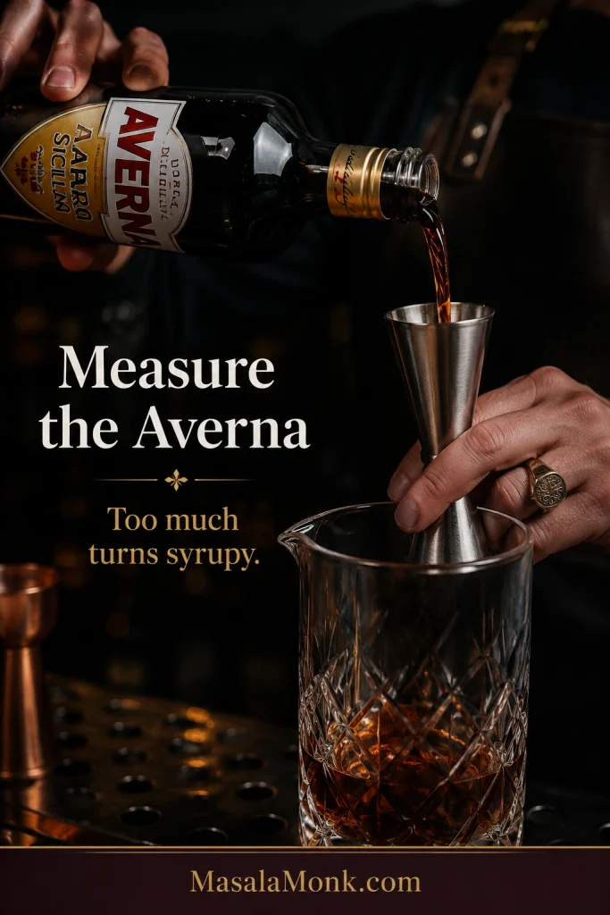 Averna amaro being measured for a Black Manhattan cocktail on a dark bar surface with cocktail tools nearby.