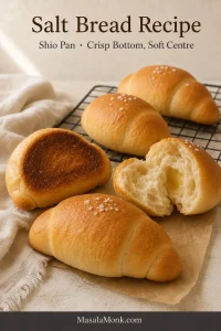 Golden crescent-shaped salt bread rolls on a cooling rack, with one roll torn open to show the crumb and another turned over to show the browned underside.