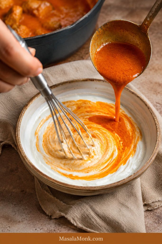 Sour cream being whisked in a bowl while hot paprika sauce is added gradually from a spoon.