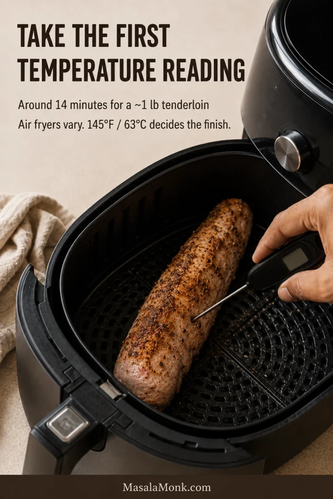 Partly browned pork tenderloin in an air-fryer basket being checked in the thickest section with an instant-read thermometer.
