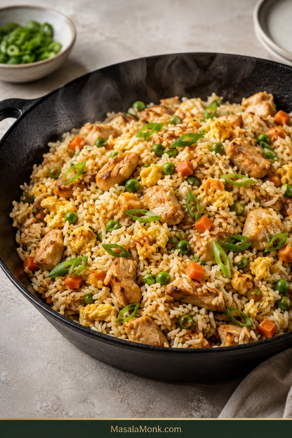 Finished chicken fried rice in a dark skillet with separate pale-golden rice grains, small browned chicken pieces, tender scrambled egg, peas, carrots and sliced scallions.