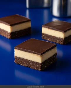 Three Nanaimo bar squares on a cobalt surface, showing a dark textured base, pale custard middle, and thin chocolate topping.