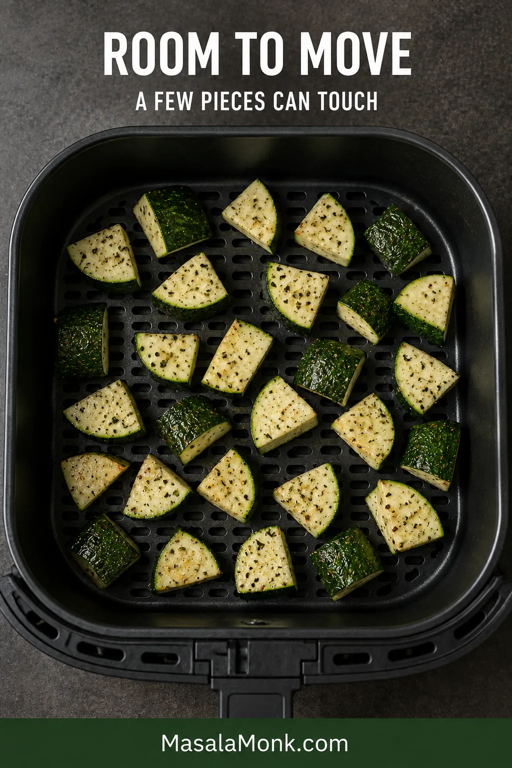 Seasoned raw zucchini chunks arranged loosely in one layer inside a perforated air fryer basket, with visible gaps and basket holes between them.