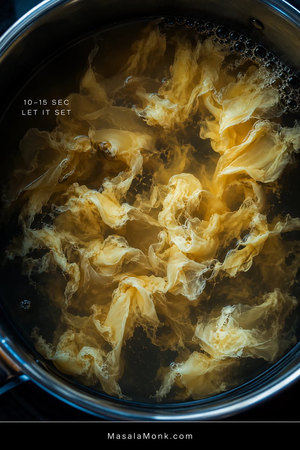 Close overhead view of pale egg ribbons blooming and setting in hot golden broth, with no spoon or stirring utensil touching the soup.