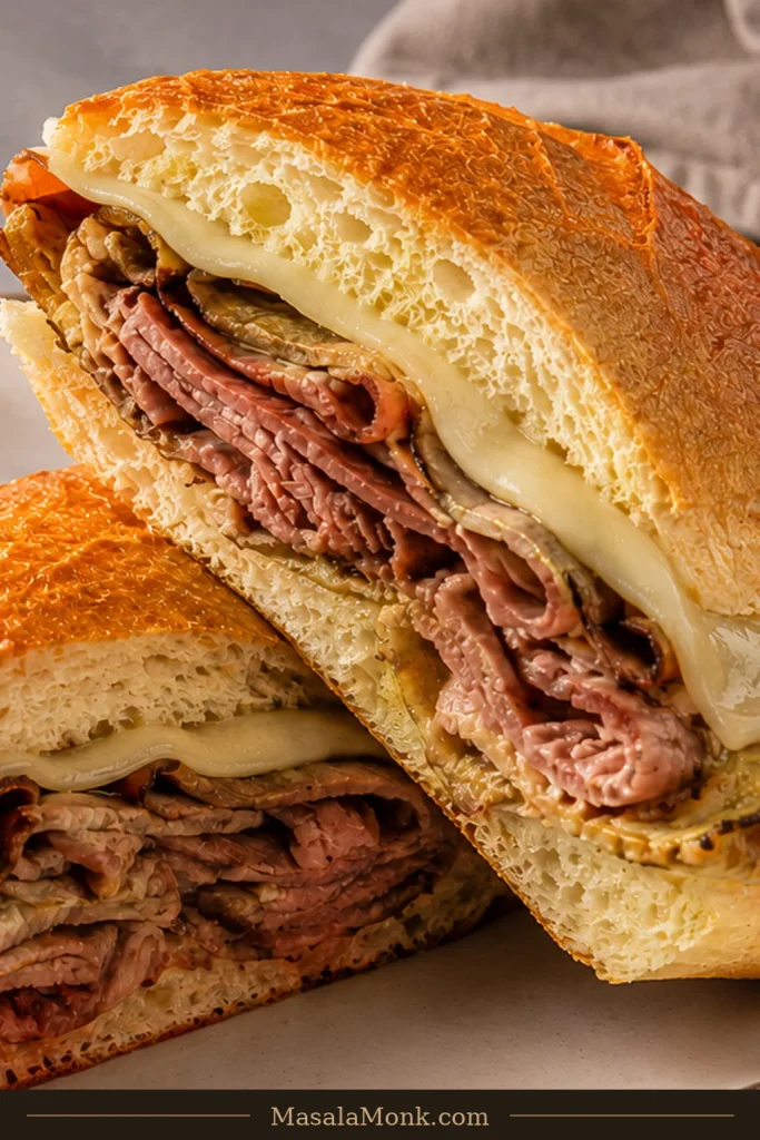 Finished French dip sandwich cut into halves on a plate beside a small ramekin of brown au jus.