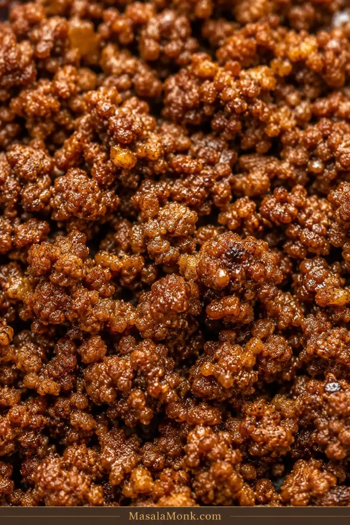 Close-up of finished seasoned taco meat with irregular browned crumbles, a light moist sheen, and no loose liquid in the pan.