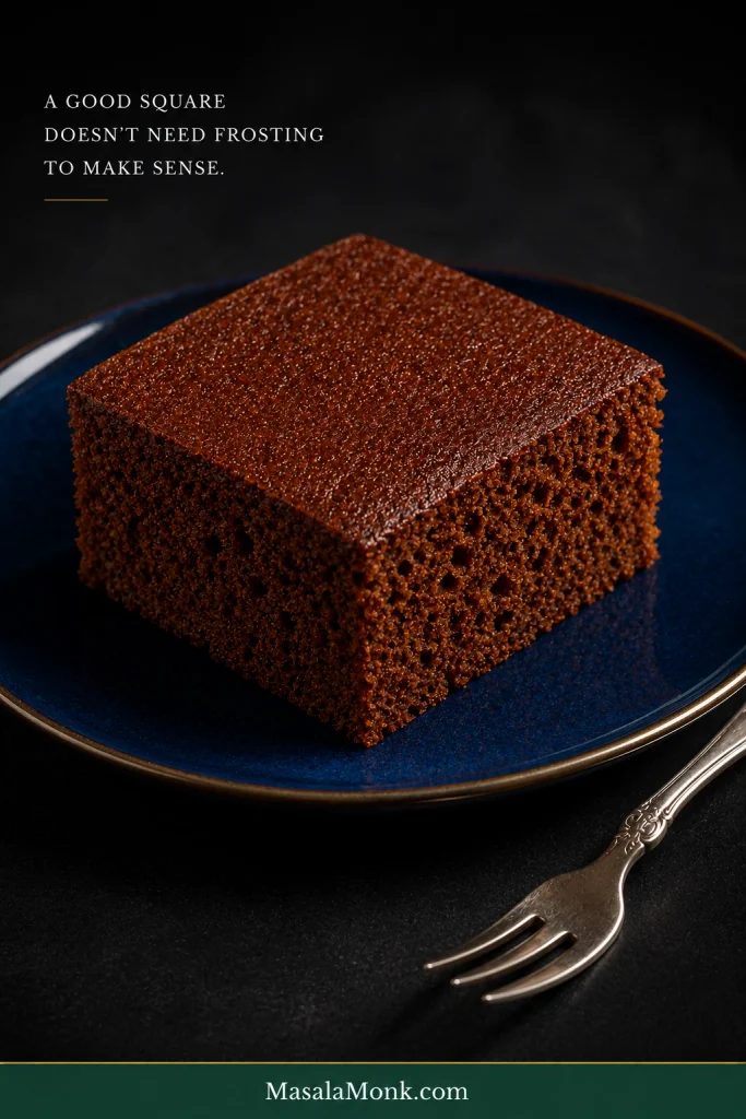 Plain unfrosted gingerbread cake square on a dark blue plate with a silver fork.