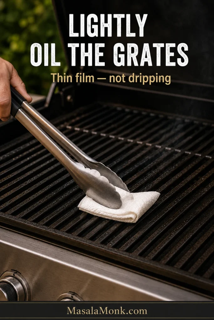 Long metal tongs holding a folded, lightly oiled paper towel while wiping clean hot grill grates.