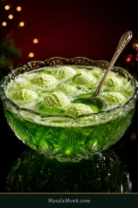 Crystal punch bowl filled with bright green fizzy punch, pale lime sherbet scoops, loose froth and a silver ladle against a dark red Christmas setting.