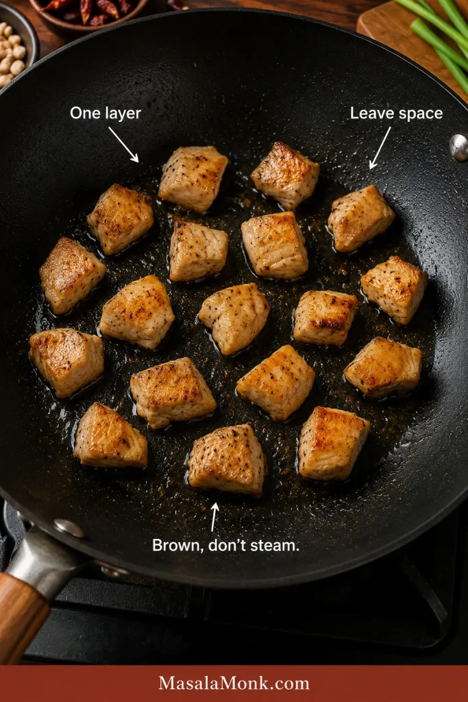 Chicken pieces browning in one layer with visible space between them in a hot pan.