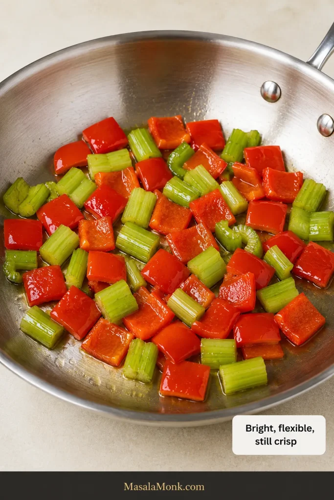 Bright red bell pepper and green celery stir-frying in a stainless-steel skillet while still crisp and structured.