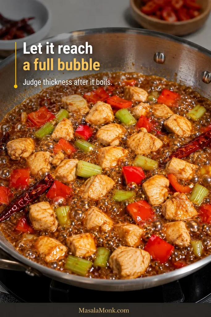 Takeout-style Kung Pao chicken, red pepper and celery in actively bubbling brown sauce before it fully thickens.