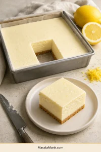 One square lifted from the centre of a pan reveals thick pale lemon filling standing above a thin golden biscuit crust.