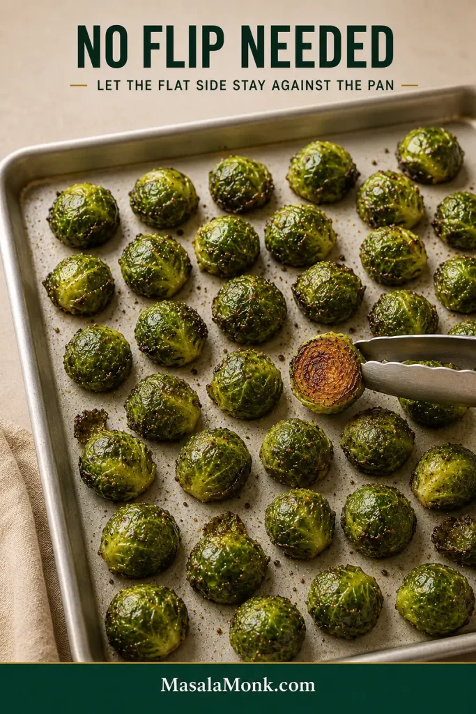 Roasted Brussels sprouts resting rounded-side up on a sheet pan while one piece is turned to reveal its dark caramelized underside.