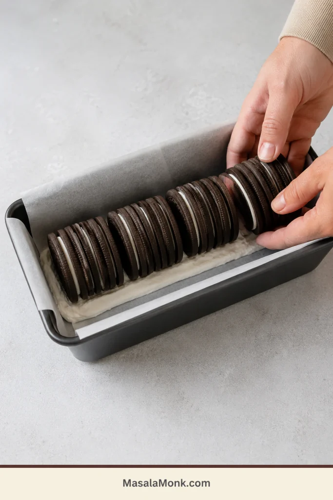 Four groups of upright thin chocolate sandwich cookies being joined along the length of a lined loaf pan.