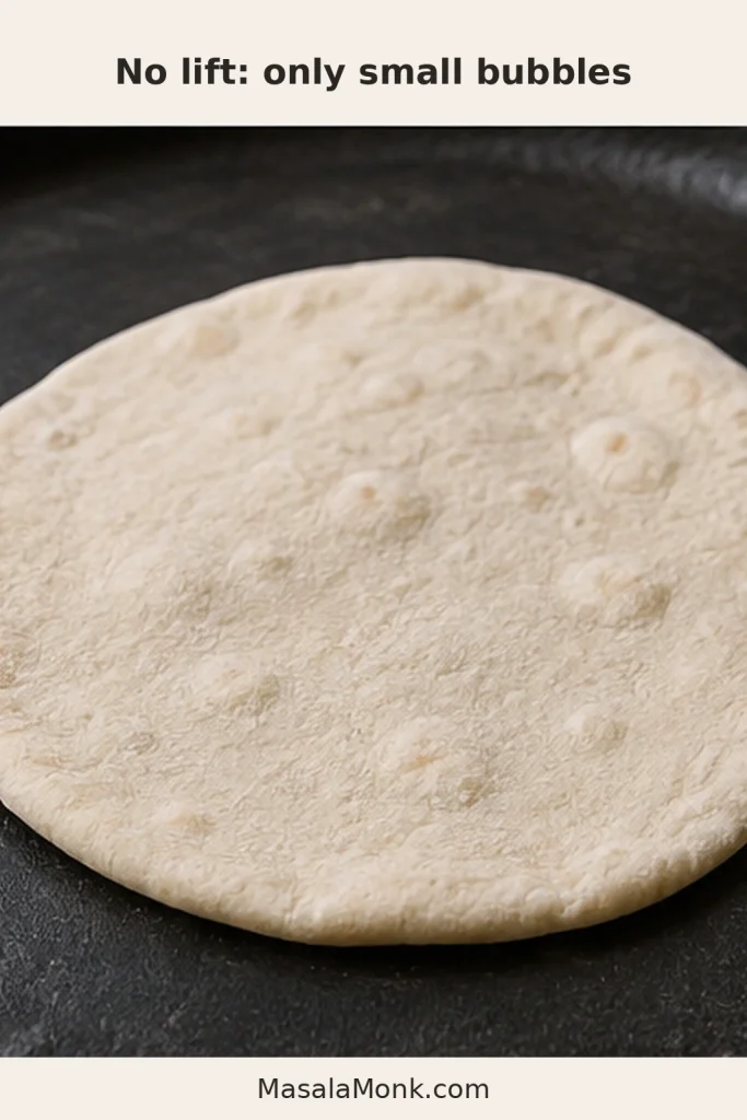 Pale cooked pita remaining flat on a dark surface with only a few small bubbles.