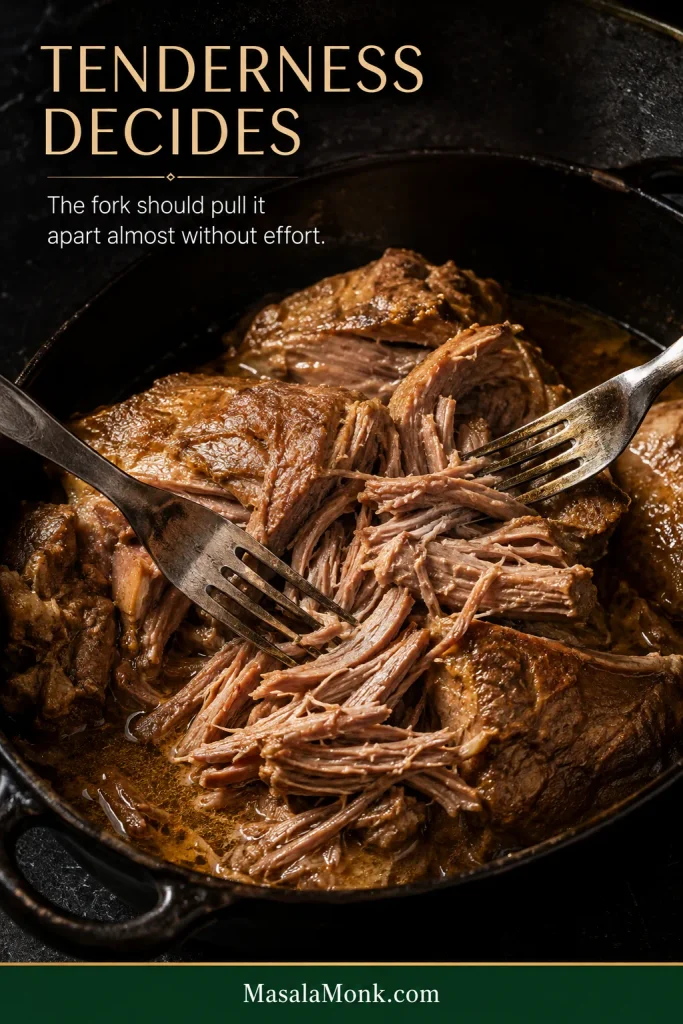Cooked pork shoulder being pulled apart easily with forks, showing moist tender strands and a light sheen of broth.
