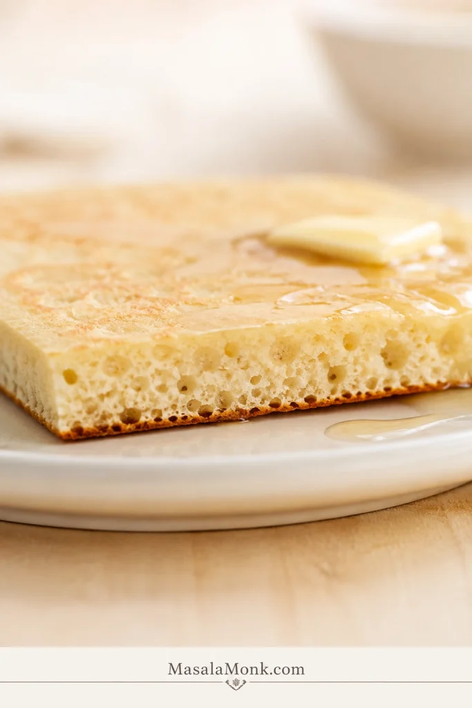 Close side view of a thin sheet-pan pancake square with a pale golden top, soft porous interior and narrow browned underside.