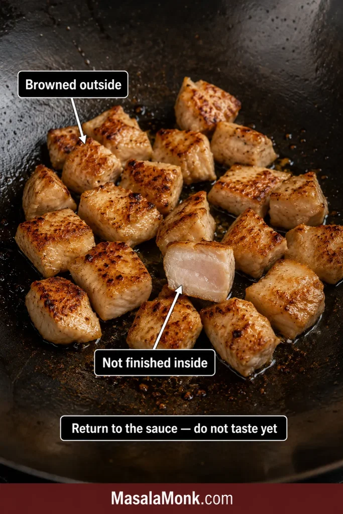 Browned chicken pieces after the first sear, with one cut piece showing a centre not yet fully cooked.