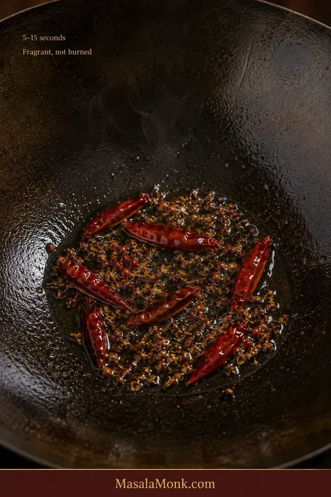 Dried red chillies and lightly cracked Sichuan peppercorn sizzling briefly in oil in a carbon-steel wok.