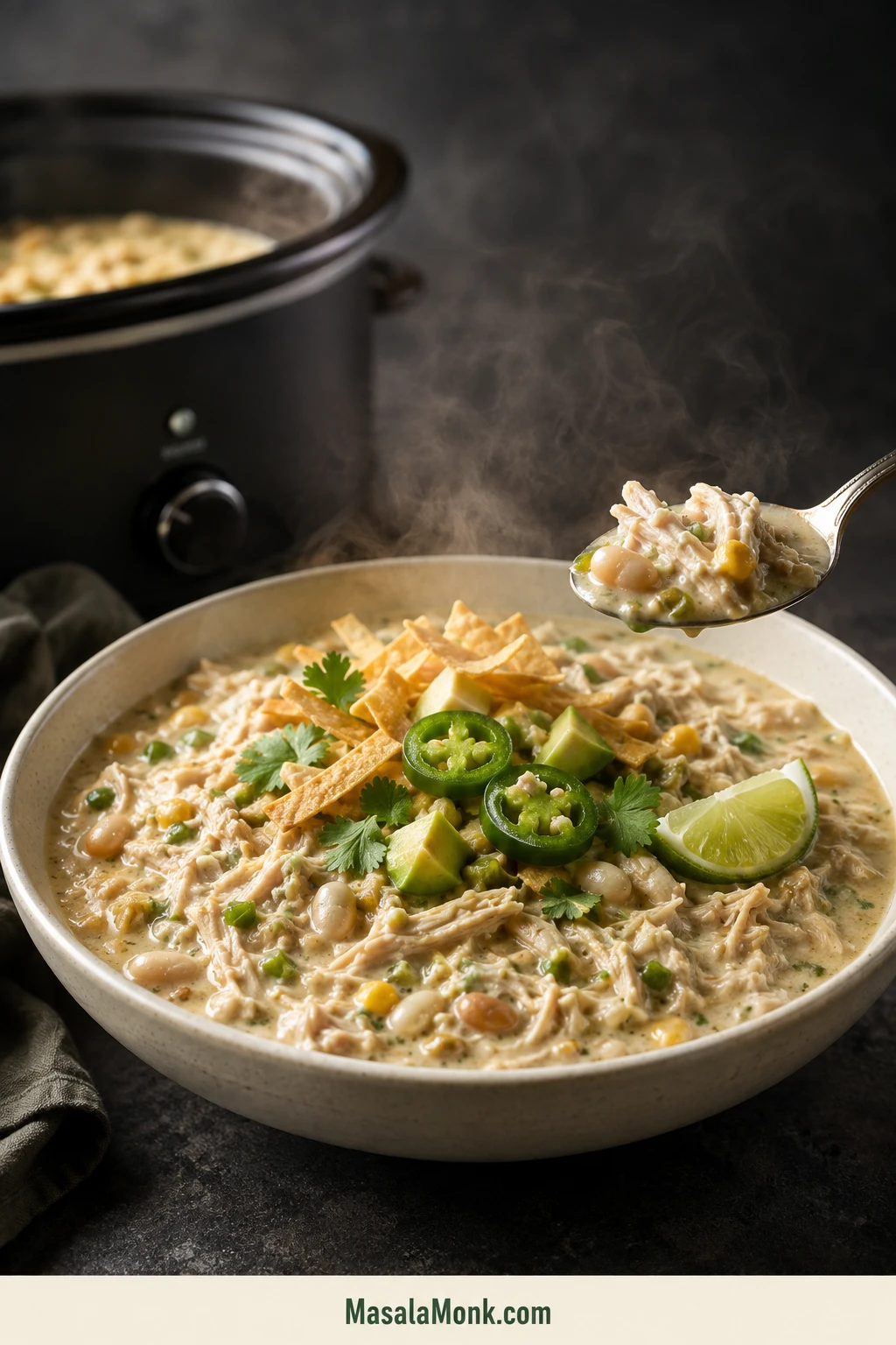 Bowl of creamy white chicken chili with shredded chicken, white beans, green chiles, corn and fresh garnishes beside the slow cooker.