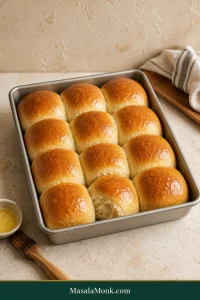 Twelve golden dinner rolls baked in four rows of three, with pale touching sides and one roll opened to show the soft interior.
