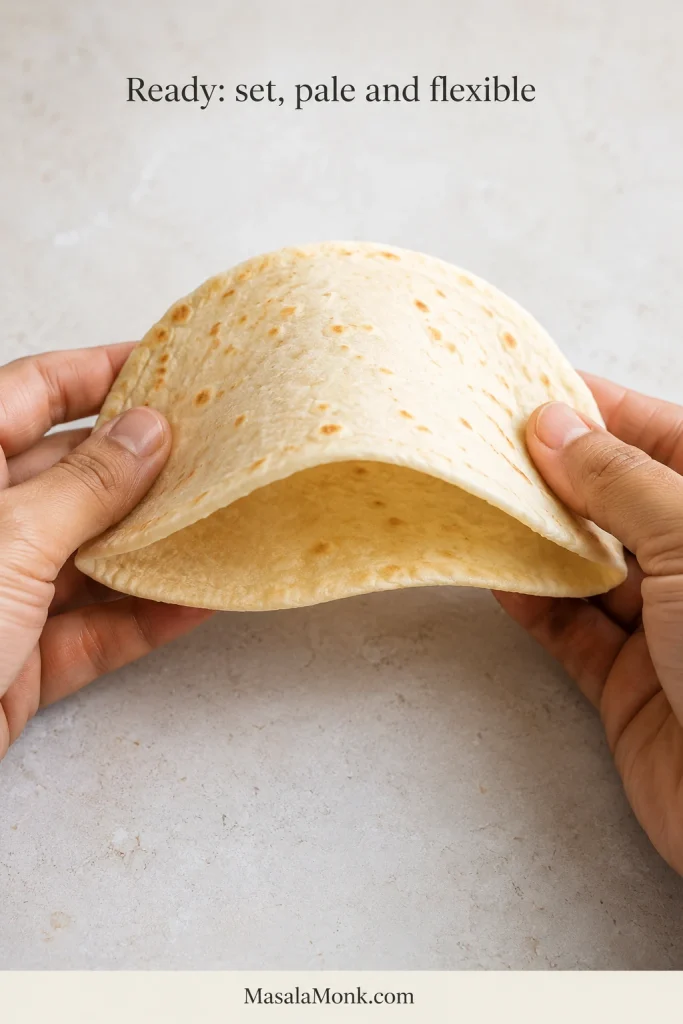 Two hands gently bending a pale cooked pita without cracking it.