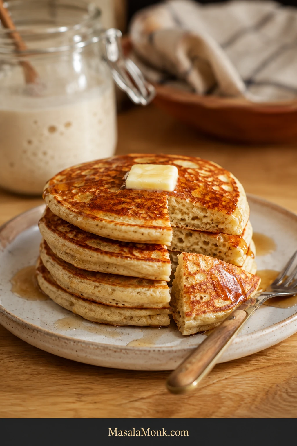 Stack of golden-brown sourdough discard pancakes with melting butter and maple syrup, with one cut pancake showing a soft cream-colored interior with small air pockets.