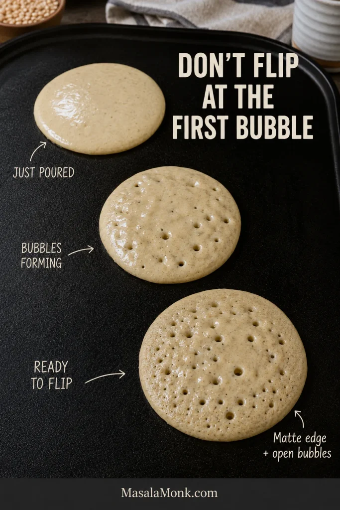 Three pancakes on one griddle show cooking stages from freshly poured batter to forming bubbles and a ready-to-flip pancake with a matte edge and open bubbles.