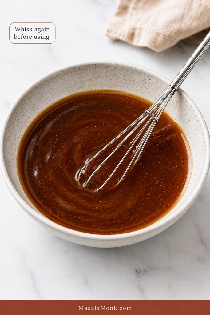 Thin brown takeout-style Kung Pao sauce being whisked in a pale bowl.