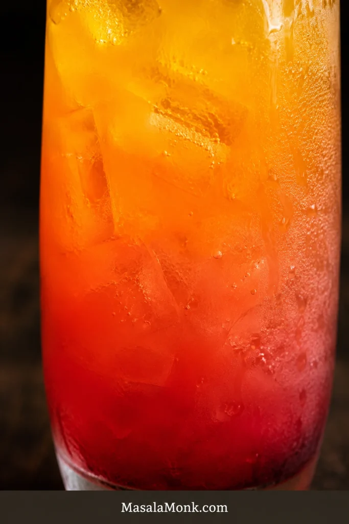 Close-up of a finished Tequila Sunrise with a red bottom, coral middle and bright orange upper layer visible through ice.