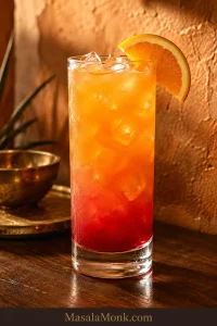 Tequila Sunrise in a tall clear glass with ice, deep red lower layer, coral fade, bright orange top and orange garnish.