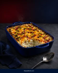 Blue rectangular casserole dish filled with fluffy potato and topped with melted cheddar, crisp bacon and sliced green onions, with a serving removed from one corner.