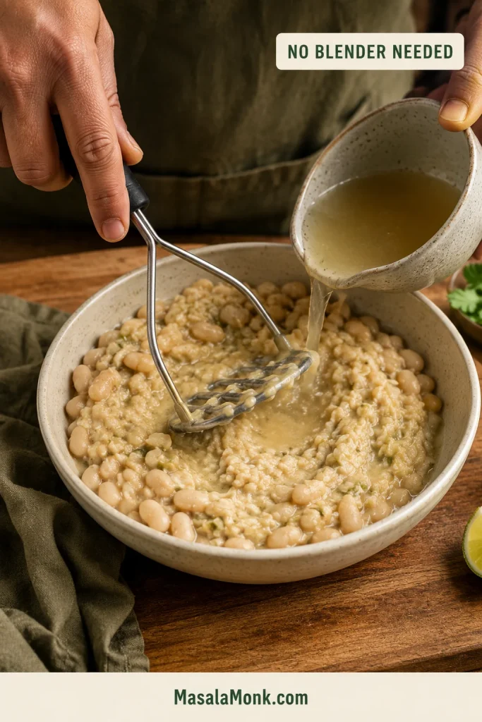 White beans being mashed by hand into a rustic paste as a no-blender thickening method.