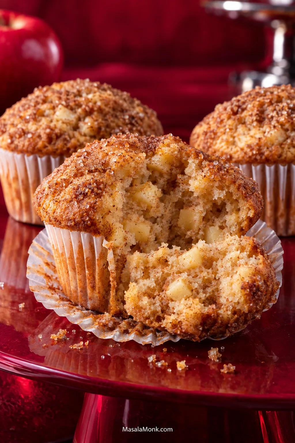 Broken-open apple cinnamon muffin with a tender golden crumb, small apple pieces throughout and a thin cinnamon-sugar crust, with whole muffins behind it.