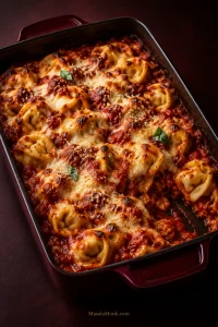 Baked cheese tortellini in red marinara with browned mozzarella and Parmesan in a dark burgundy rectangular baking dish.
