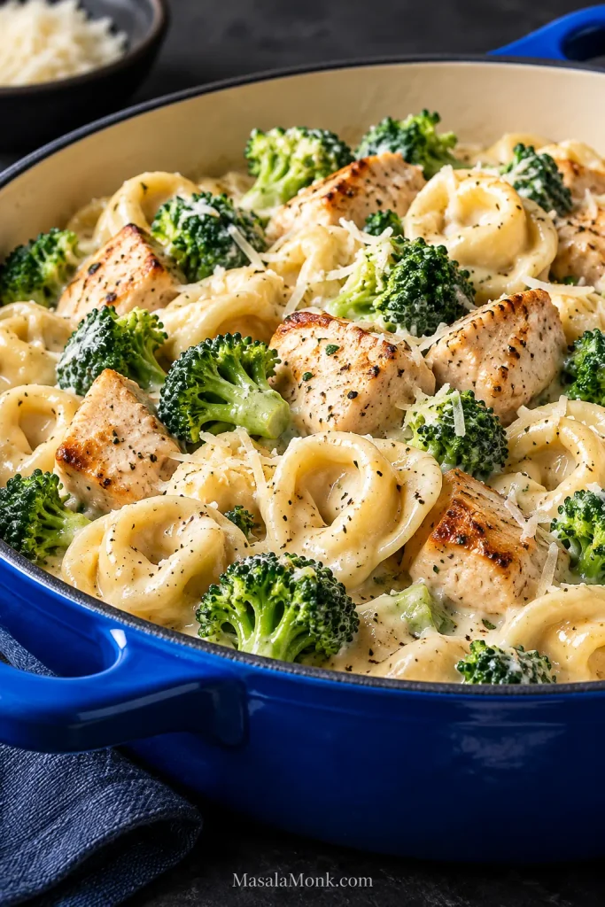 Creamy chicken tortellini Alfredo with bright green broccoli florets and browned chicken in a glossy blue serving vessel.