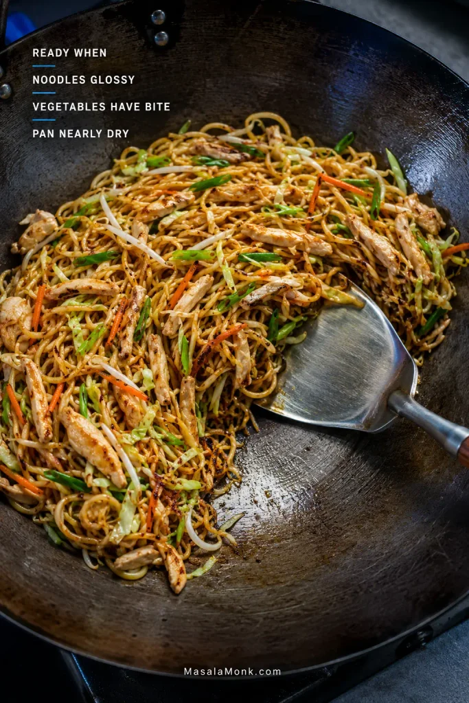 Finished chicken chow mein in a wok with separate glossy noodles, thin chicken strips, cabbage, bean sprouts, carrots and scallions, with little visible liquid underneath.