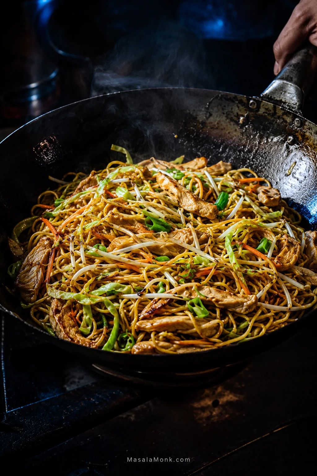 Chicken chow mein in a dark carbon-steel wok with thin chicken strips, medium-thin noodles, green cabbage, bean sprouts, carrots and scallions, with glossy strands and scattered browned edges.