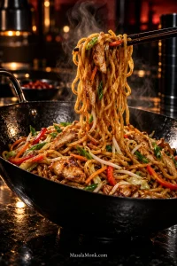 Dark chopsticks lift steaming chicken lo mein noodles from a black wok with thin sliced chicken, red bell pepper, carrots, bean sprouts and scallions.